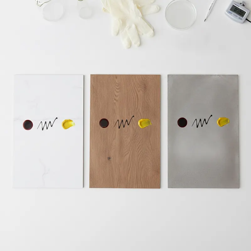 A top-down photo of a flooring experiment showing porcelain tile, luxury vinyl, and concrete samples, each with red wine, permanent marker, and mustard stains applied for a durability test.